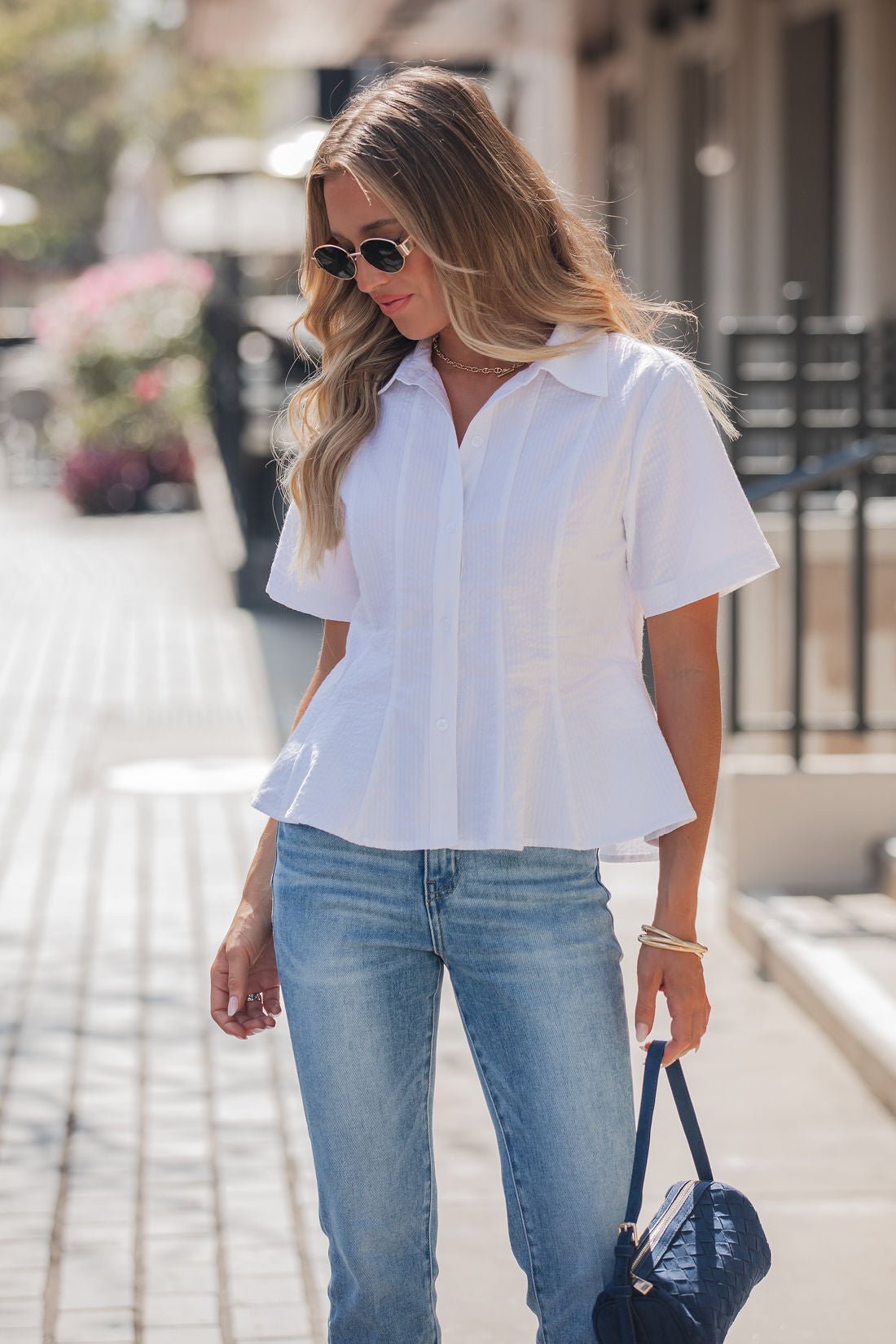 Woman with long blonde hair in sunglasses and blue jeans wearing the Steve Madden White Porter Top, standing outdoors.