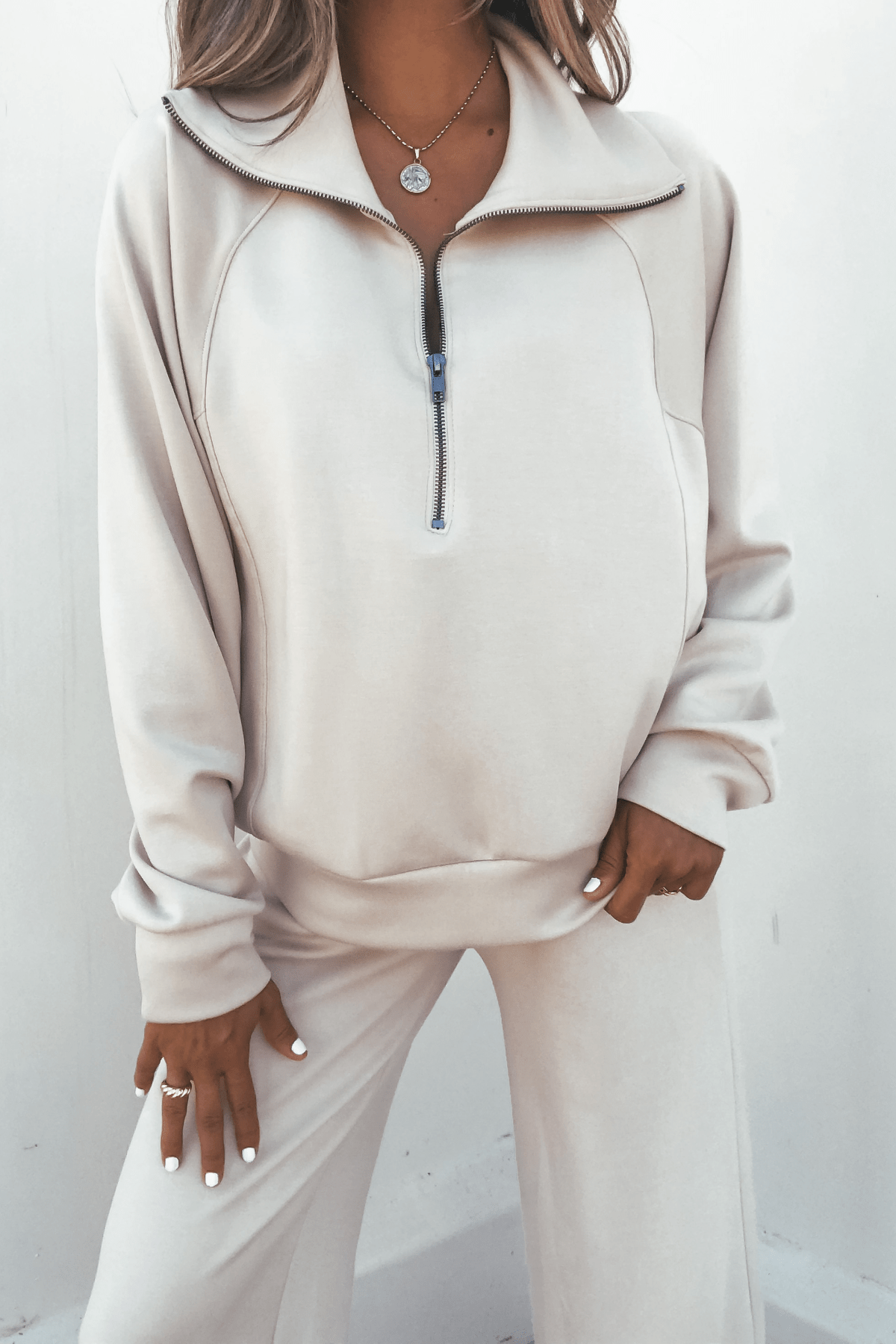 Woman wearing a relaxed fit Stone Half Zip Scuba Sweatshirt and matching pants, styled with layered necklaces and rings.