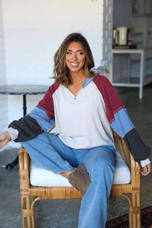 Woman with shoulder-length brown hair smiles in a modern room, wearing the Stone Multi Color Block Ribbed Pullover.