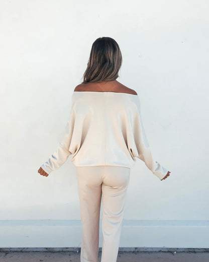 A person with long hair faces a white wall, wearing the Stone Off The Shoulder Scuba Top and matching lounge pants.