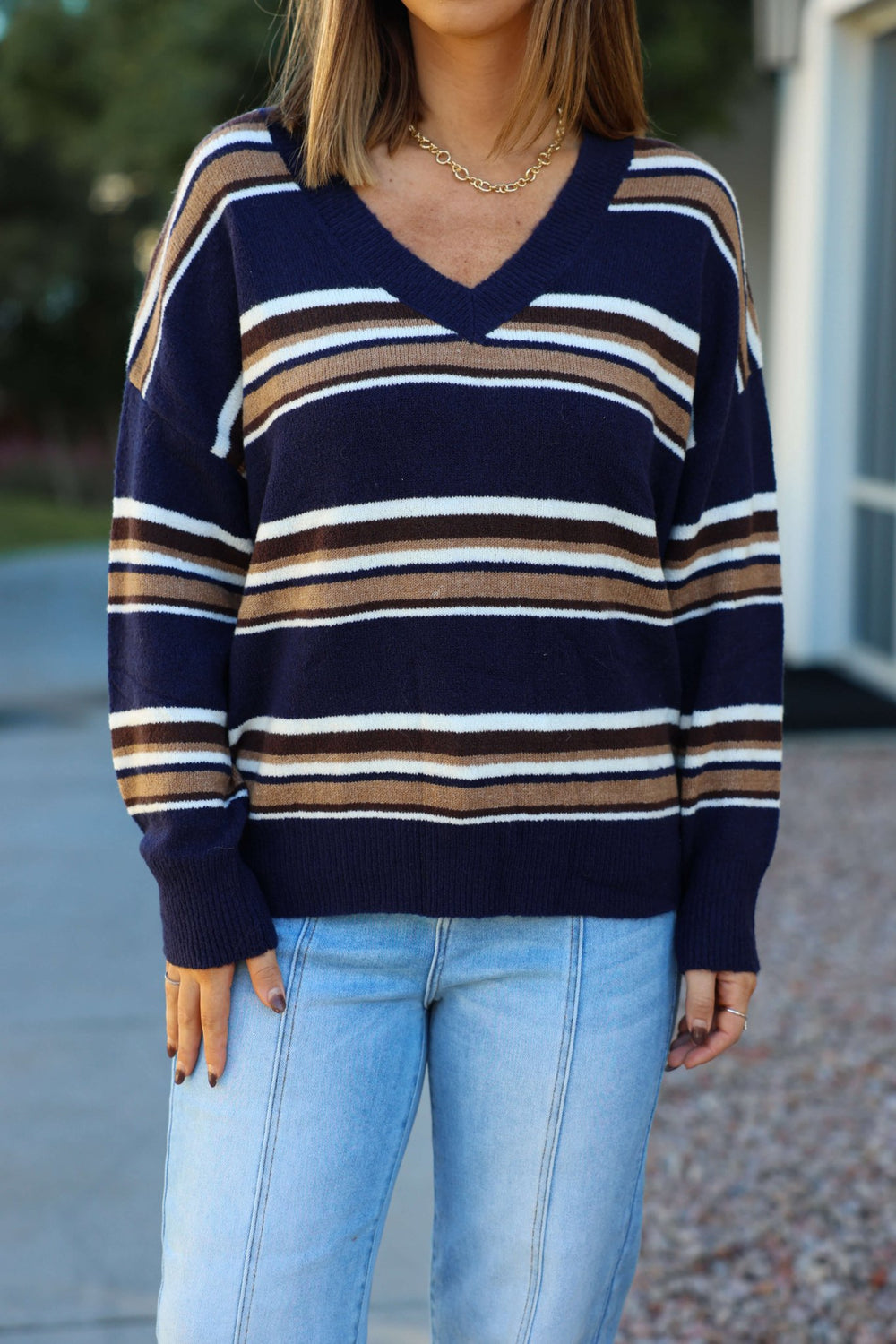 Woman wears the Street Chic Multi Navy Striped Sweater with light blue jeans while standing outdoors.