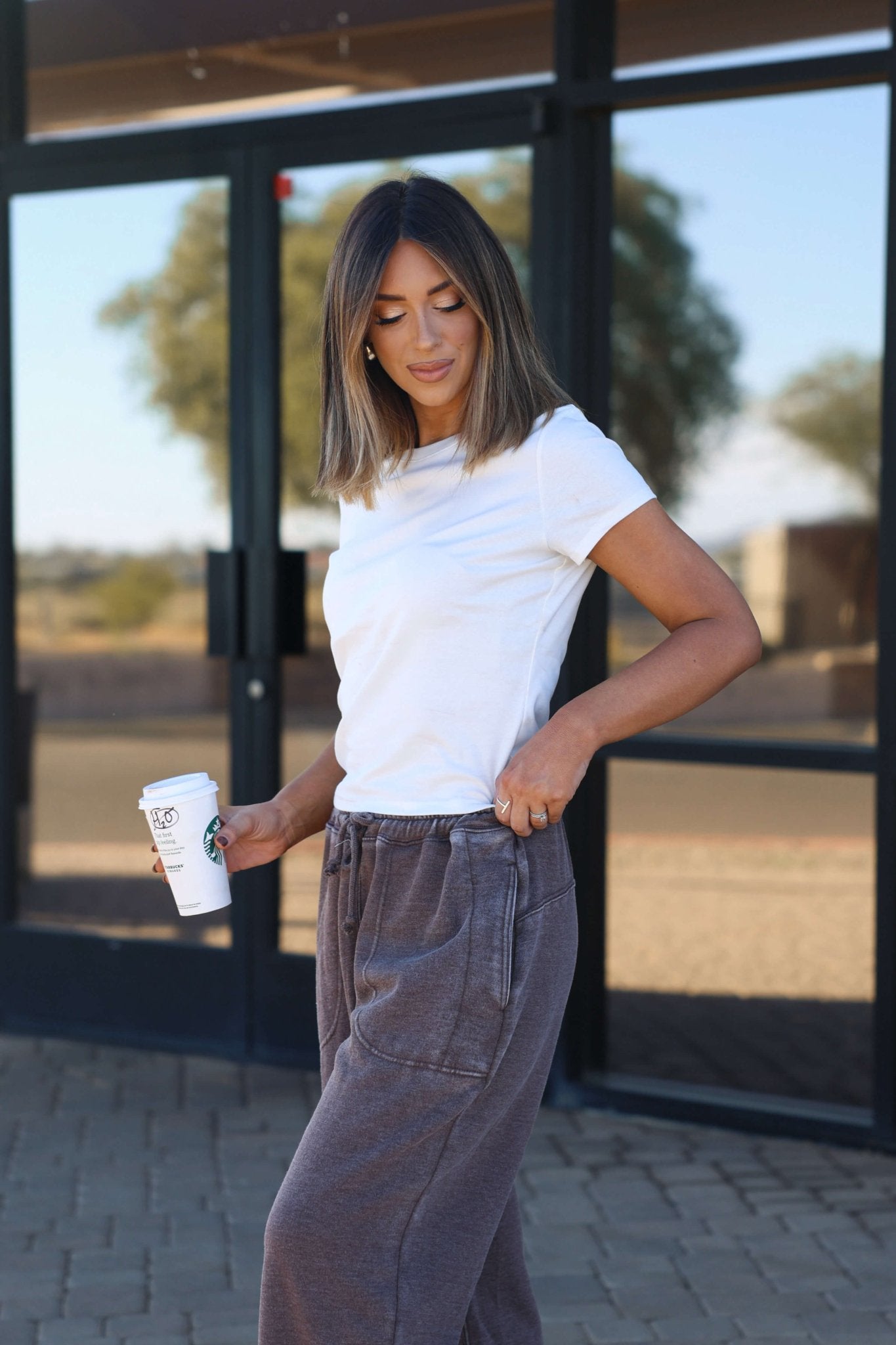 Woman in a Stretch Cotton Short Sleeve Tee - White (DOORBUSTER) and gray sweatpants holds a coffee cup outdoors.