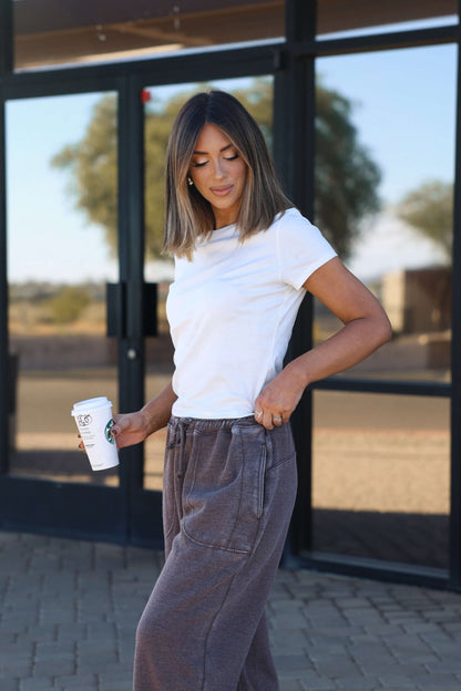 Woman in a Stretch Cotton Short Sleeve Tee - White (DOORBUSTER) and gray sweatpants holds a coffee cup outdoors.