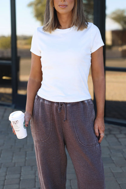 A woman in a white Stretch Cotton Short Sleeve Tee - DOORBUSTER holds a coffee cup while standing outside on pavement.