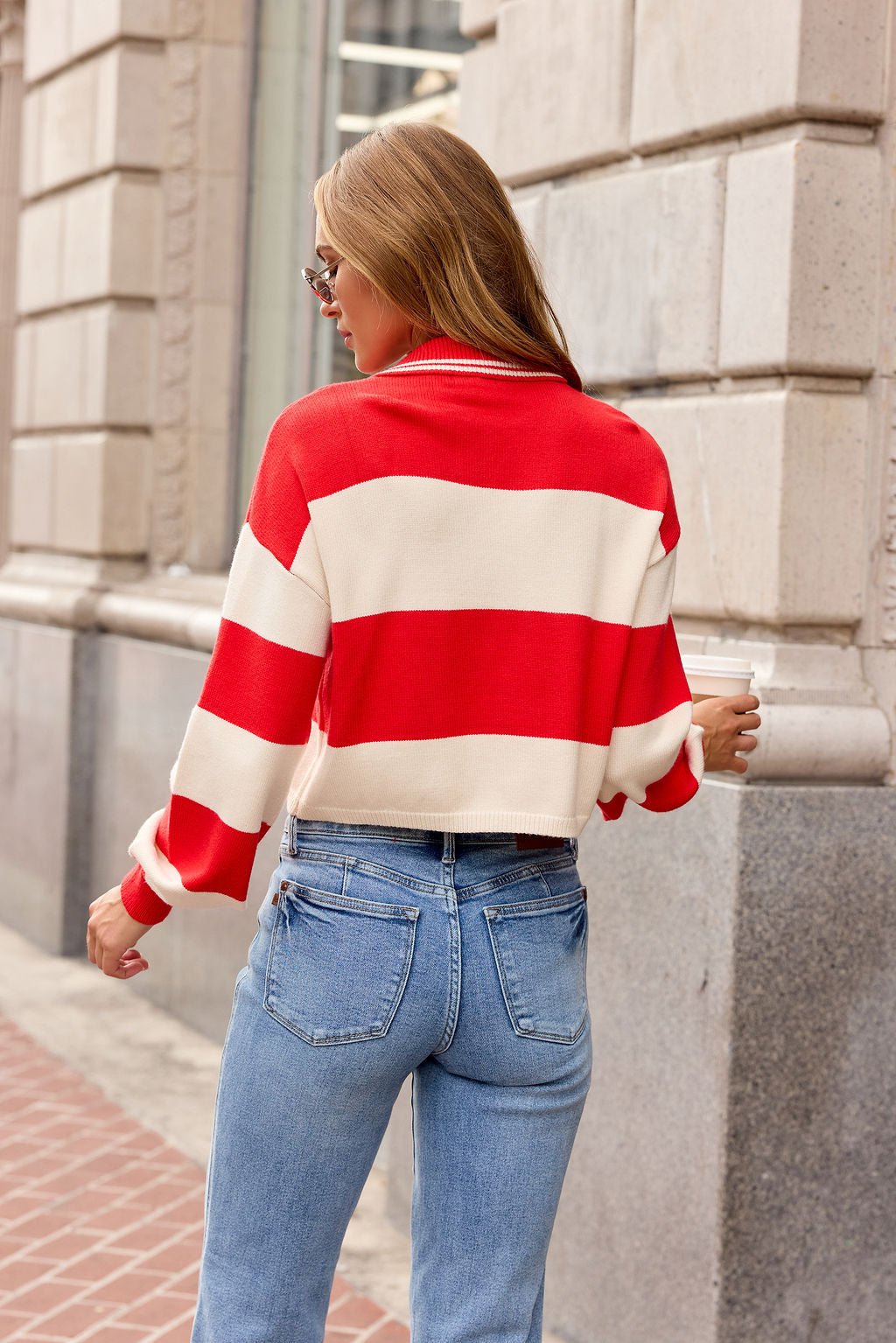 Woman with long hair wears the Striped Button Up Sweater - Red on a city sidewalk, facing away from the camera. Pre-order now!.