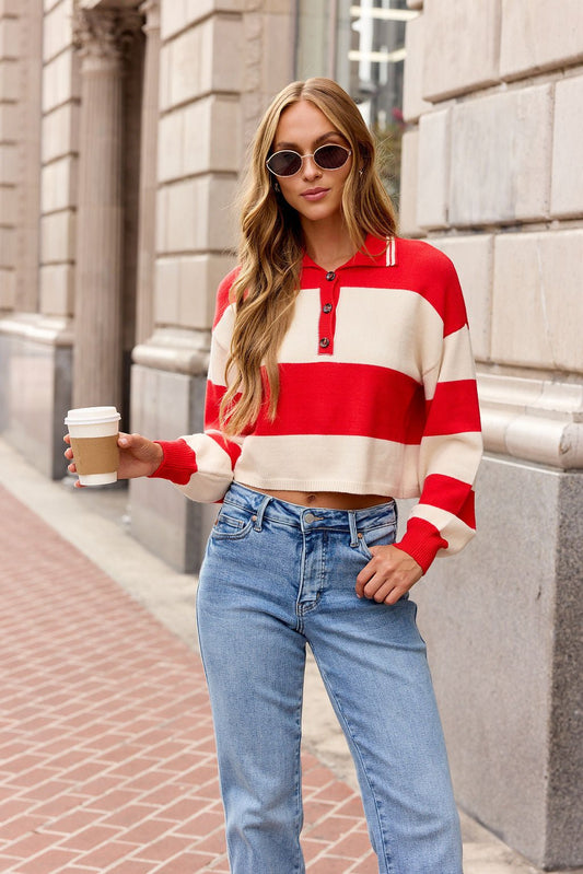 Woman wearing the Striped Button Up Sweater - Red | Pre Order, blue jeans, and sunglasses holds coffee on a city sidewalk.