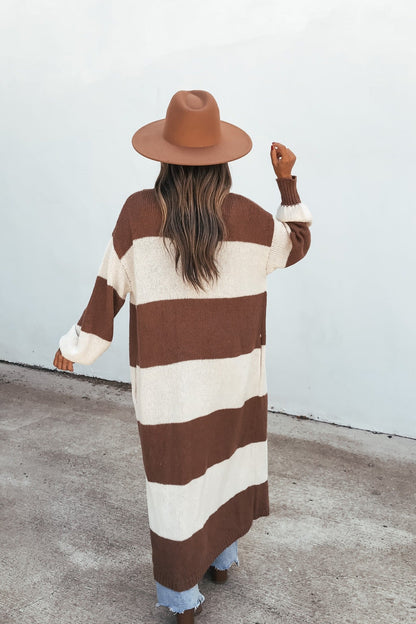 Woman wears the Striped Duster Cardigan - Brown, standing on pavement with her back to the camera, facing a white wall.