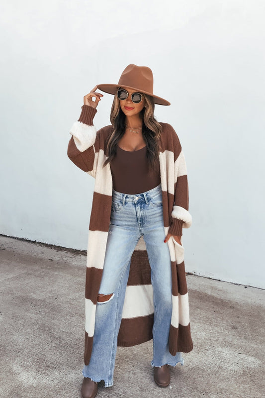 Woman in a brown hat, sunglasses, Striped Duster Cardigan - Brown, brown top, ripped jeans, and boots stands on concrete.