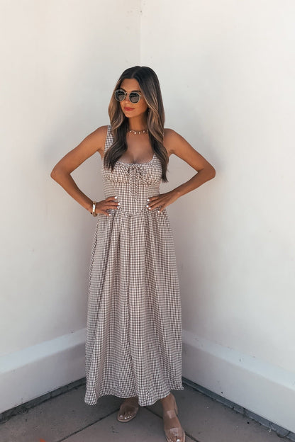 Woman in Sunfield Gingham Corset Midi Dress - Brown wears sunglasses, standing against a white wall with hands on hips.