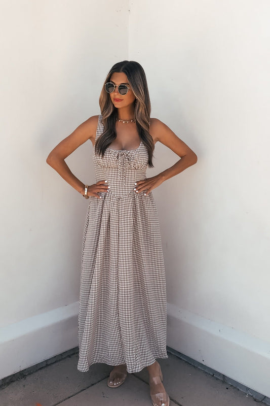 Woman in Sunfield Gingham Corset Midi Dress - Brown wears sunglasses, standing against a white wall with hands on hips.