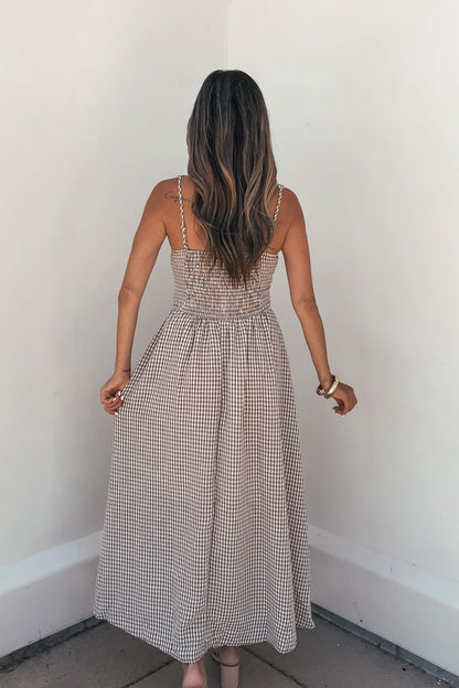 Woman with long wavy hair wears a Sunfield Gingham Corset Midi Dress - Brown, standing with her back to the camera in a corner.