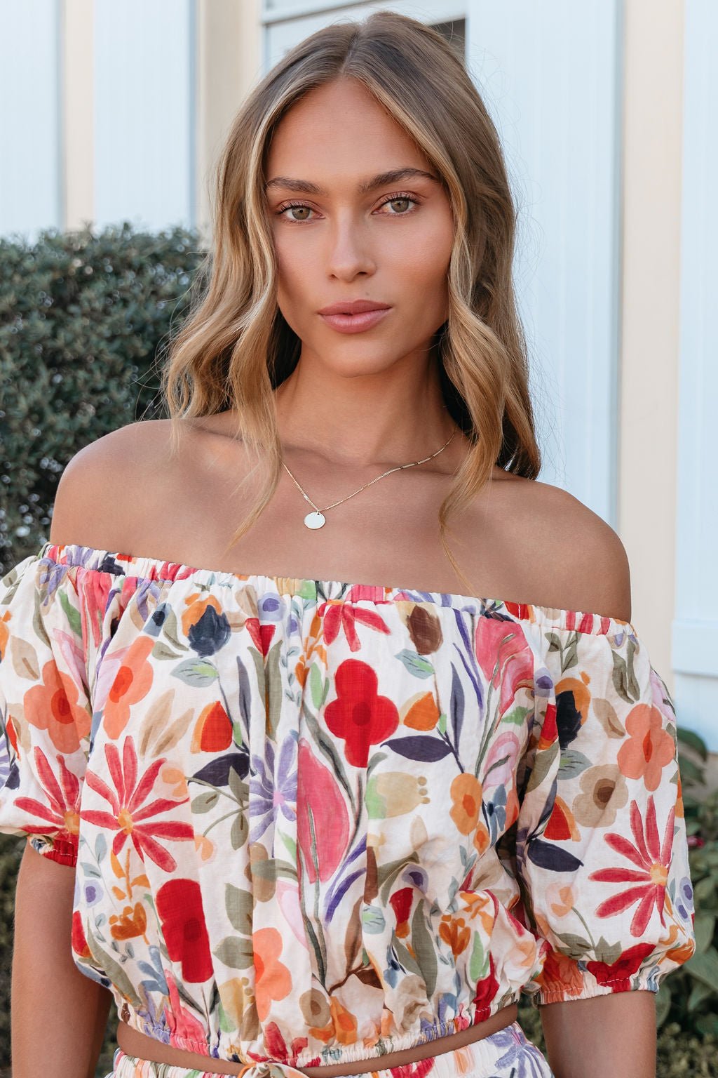 Woman with wavy blonde hair wears the Sunset Bloom Multi Print Bubble Hem Top, standing outside and calmly looking at the camera.