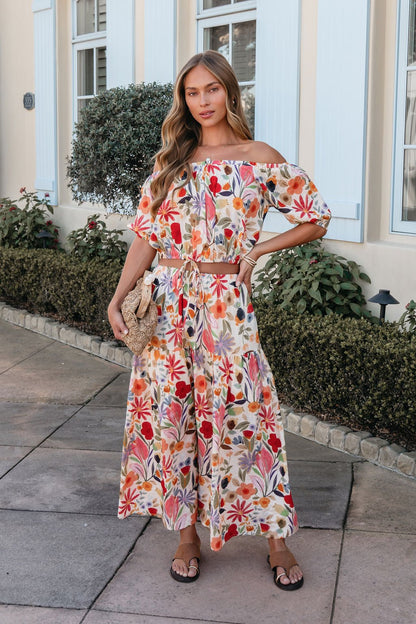 Woman stands outside in the Sunset Bloom Multi Print Tiered Maxi Skirt with an elastic waistband, holding a straw bag.