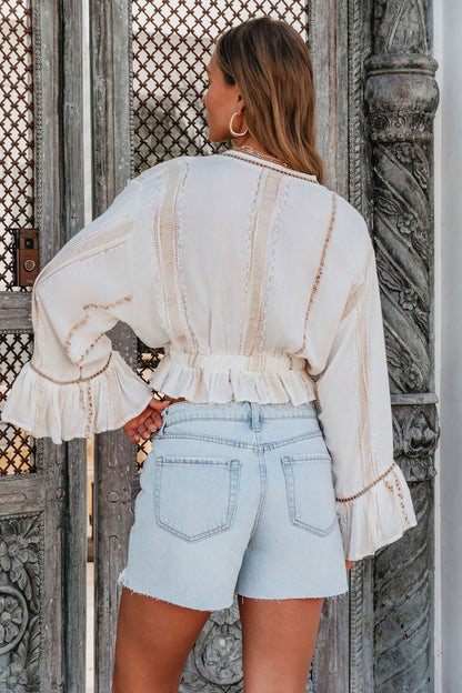 A woman with wavy hair, seen from behind, wears the Surf Gypsy Gold Dust Stripe Tie Blouse and light denim shorts.