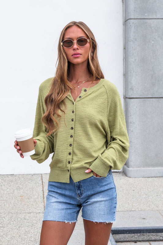 Woman in sunglasses wears the Sutherlin Button Front Top - Green with denim shorts, holding a coffee cup outdoors.