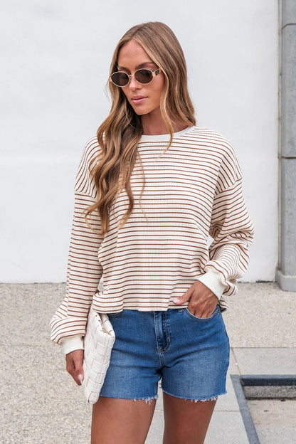 Woman in sunglasses wears the Sutton Striped Pullover - Cream and denim shorts, holding a white clutch outdoors.