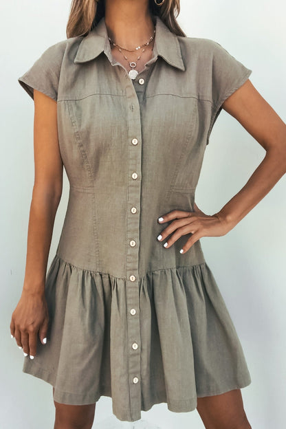 Woman in the Sweet Escape Linen Mini Dress - Olive, short-sleeve, button-down, flared skirt, posing with hand on hip and layered necklaces.