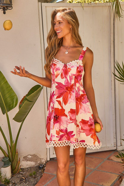 A woman in the Sweet Orchard Print Mini Dress - Pink smiles while holding and tossing lemons outdoors among plants.