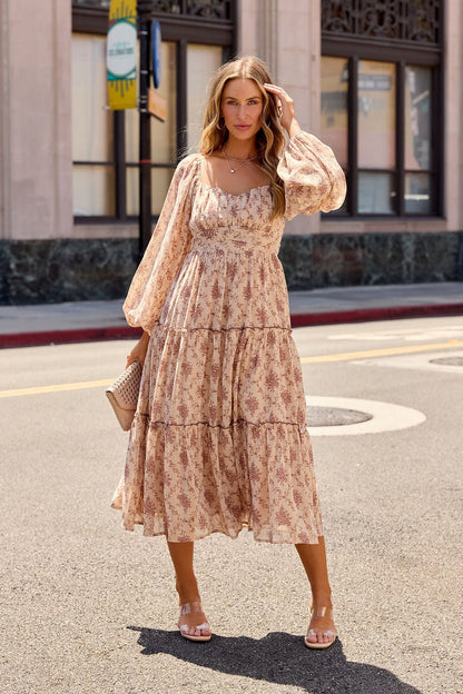 Woman in the Sweetheart Floral Print Midi Dress - Sand stands on a sunny city street, holding a beige clutch.