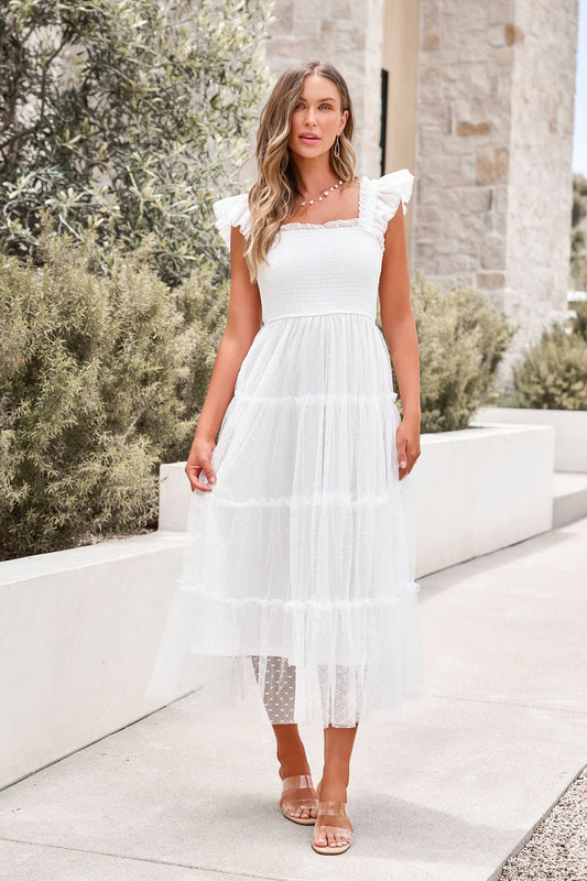 Woman in a Swiss Dot Tulle Midi Dress - White and sandals stands outdoors by stone walls and greenery.
