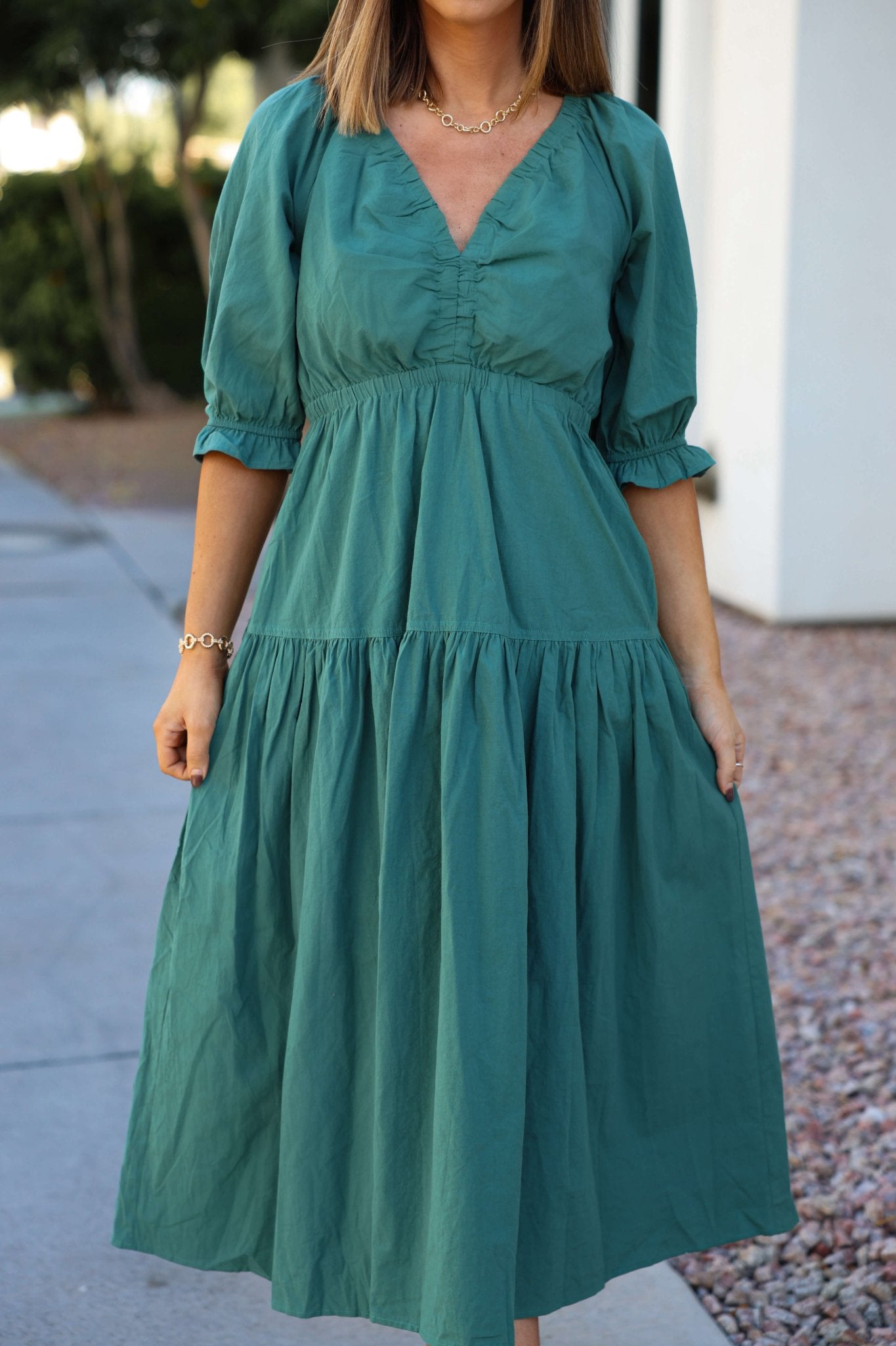 A woman stands outside wearing the Teal Puff Sleeve Tiered Midi Dress near a building and rocks.