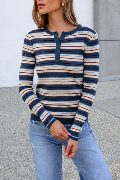 Woman in a Teal Striped Henley Long Sleeve Top and light blue jeans stands outdoors against a neutral background.