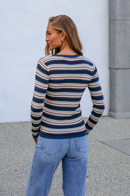 Woman in a relaxed fit teal striped henley long sleeve top and light blue jeans stands outdoors on a paved surface.