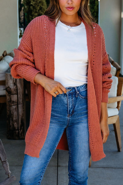 Woman in a white t-shirt, blue jeans, and a Terracotta Open Front Cardigan, standing indoors.
