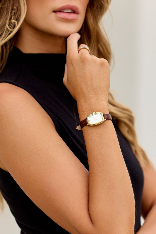 Woman wearing a sleeveless black top and The Colette Leather Watch - Brown, resting her hand near her chin.