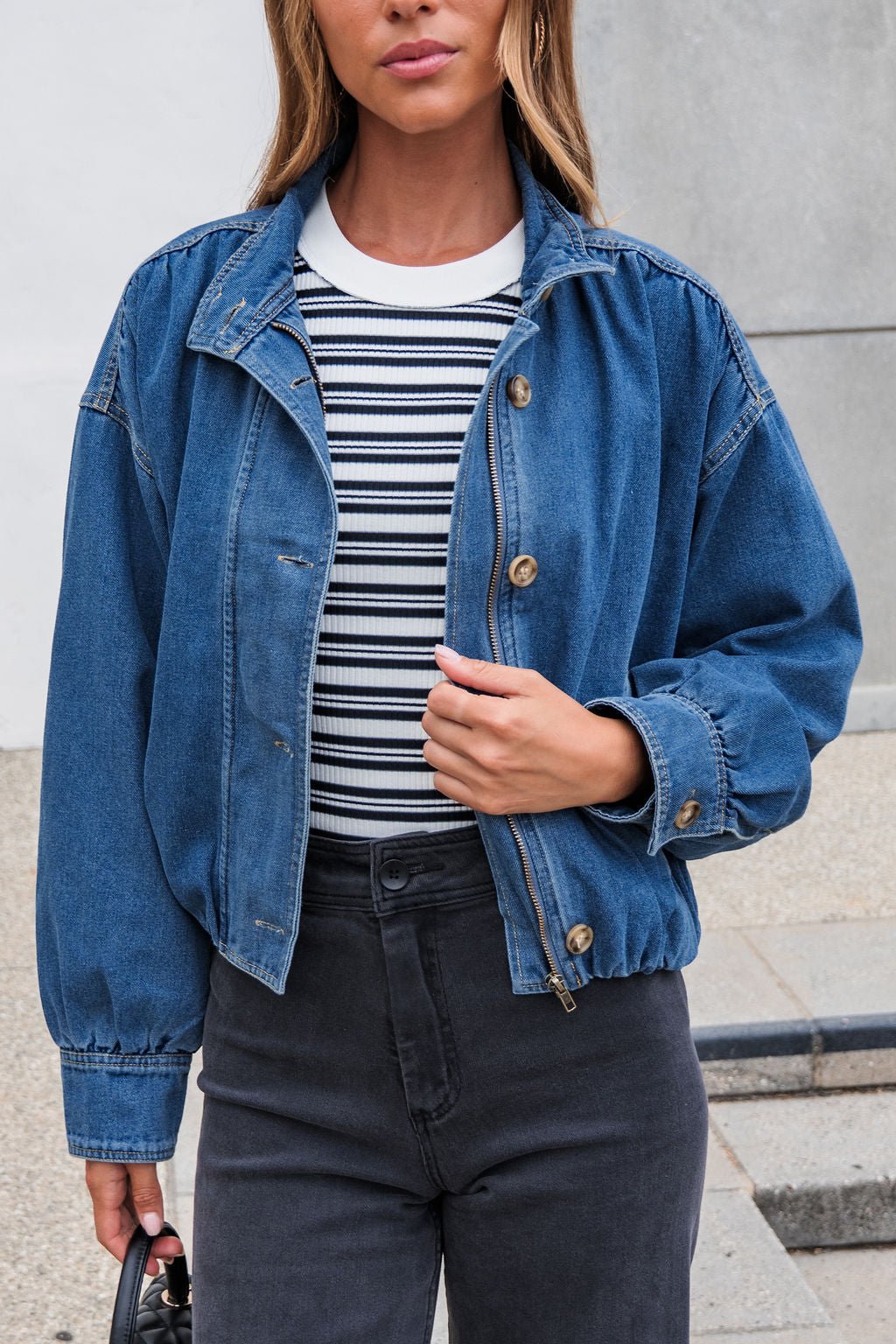Woman outdoors wearing The Dakota Denim Jacket with a collared neckline over a striped shirt, holding the jacket open.