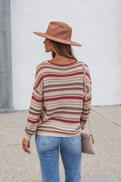 Woman in The Delaney Striped Sweater - Rust, jeans, and brown hat stands outside, holding a quilted purse with her back to the camera.
