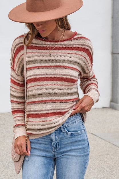 Woman in The Delaney Striped Sweater - Rust, light blue jeans, and wide-brim hat stands outdoors, face partly hidden by the hat.