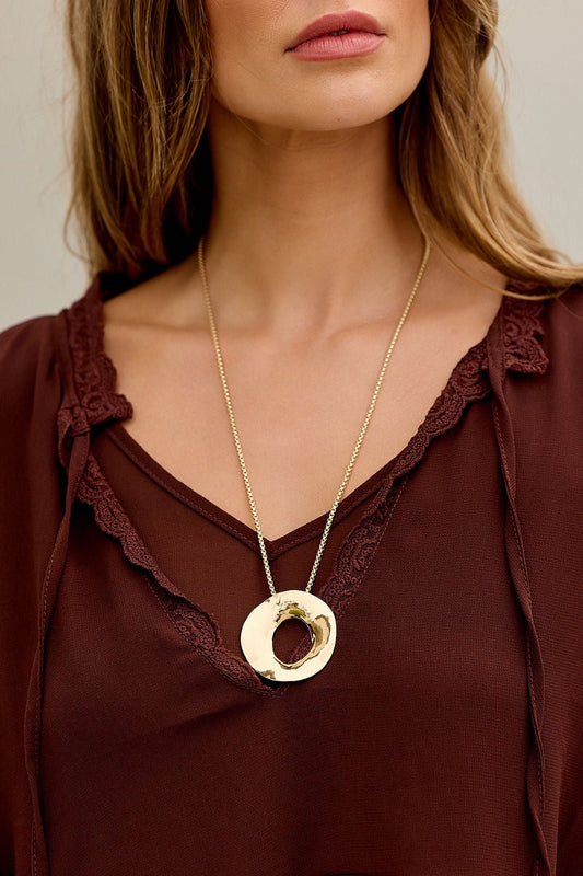 Woman in maroon blouse wears The Eclipse Pendant Necklace - Gold, featuring a sculptural open circle on a large gold chain.