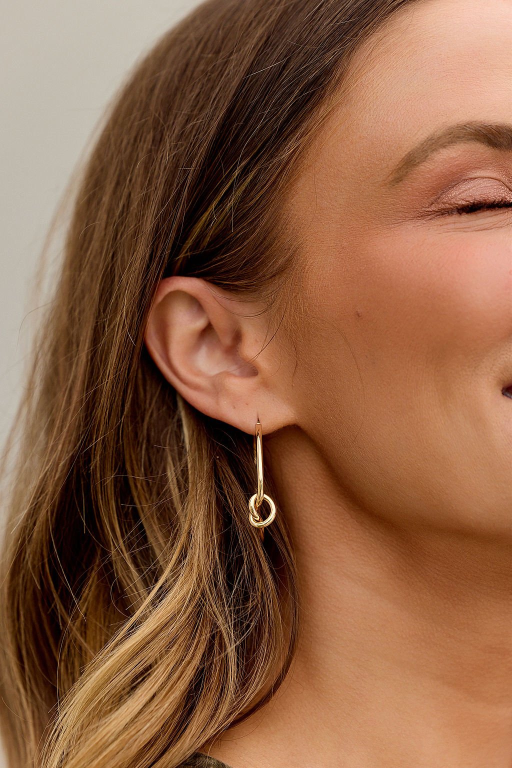 Close-up of a woman's ear with The Elara Hoop Earrings - Gold and wavy brown hair.