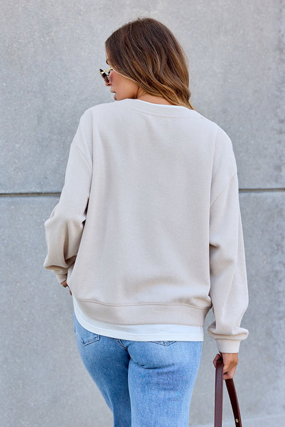 Woman wearing The Everyday Pullover - Clay and blue jeans stands with her back to the camera, holding a brown bag against a gray backdrop.