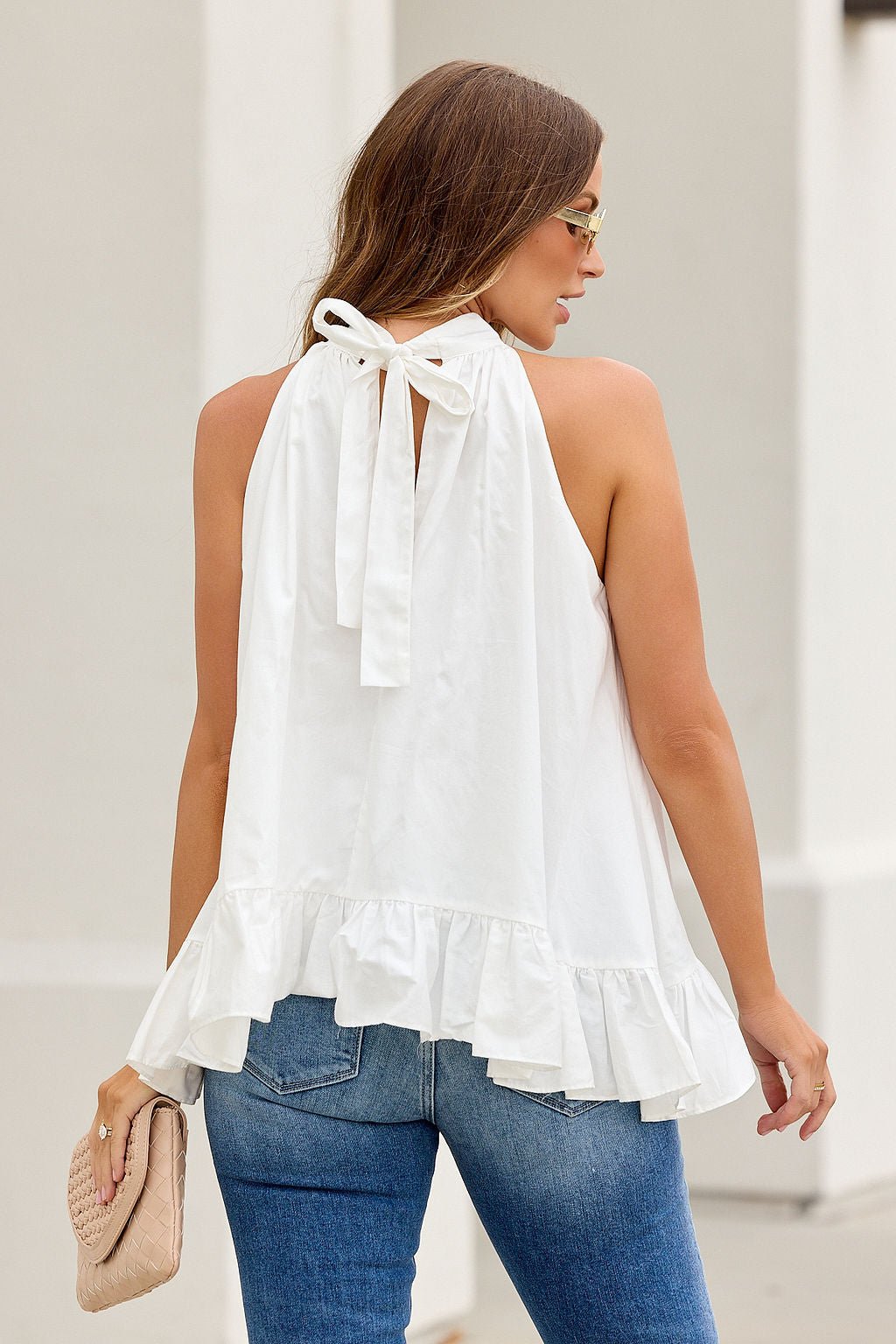 Woman in jeans and The Harlow Ruffle Top - White, holding a clutch, standing outdoors.