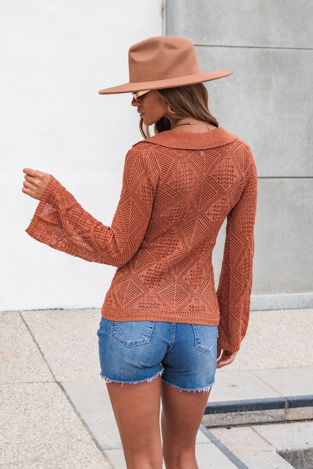 Woman in The Marisol Crochet Top - Terracotta stands outdoors; its open knit style is perfect as a beach cover up over denim shorts.
