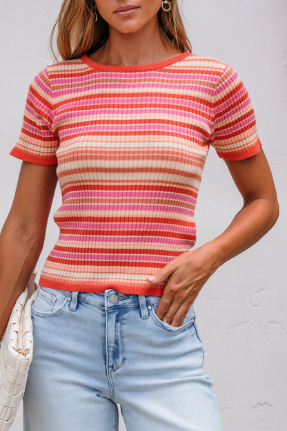 Woman in The Piper Striped Tee - Pink with light blue jeans, standing by a white wall.