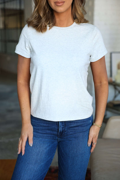 Woman wears a Thread and Supply Basic Grey Tee with a classic round neckline and blue jeans, standing indoors with relaxed hands.