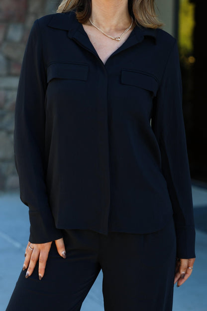 A woman wears the Thread and Supply Black Button Down Top and matching pants outdoors, styled chicly against a stone wall.