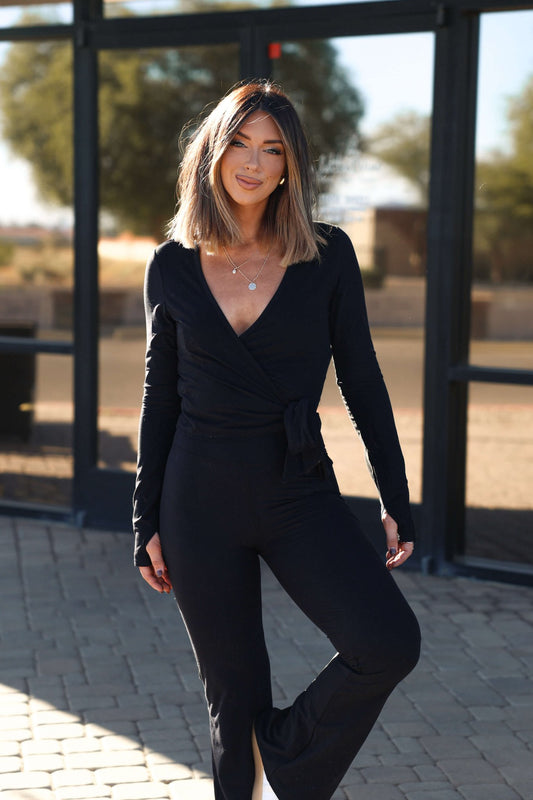 Smiling woman with shoulder-length hair wears the Thread and Supply Black Cross Front Top and pants, standing on a stone walkway.
