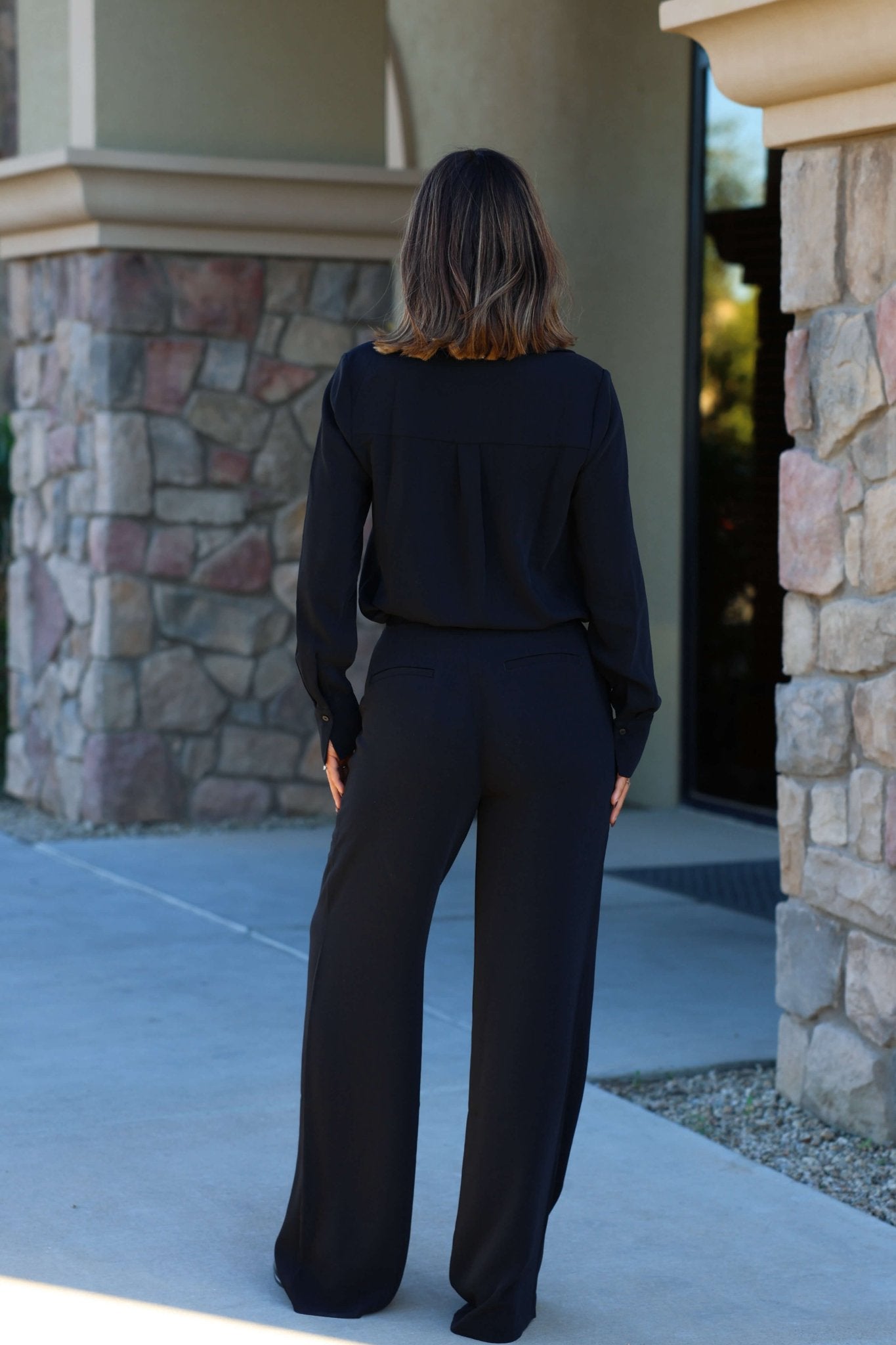A woman stands outdoors with her back to the camera in Thread and Supply Black Dress Pants featuring a pull-on elastic waistband.