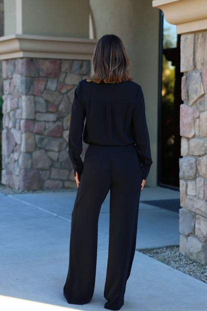 A woman stands outdoors with her back to the camera in Thread and Supply Black Dress Pants featuring a pull-on elastic waistband.