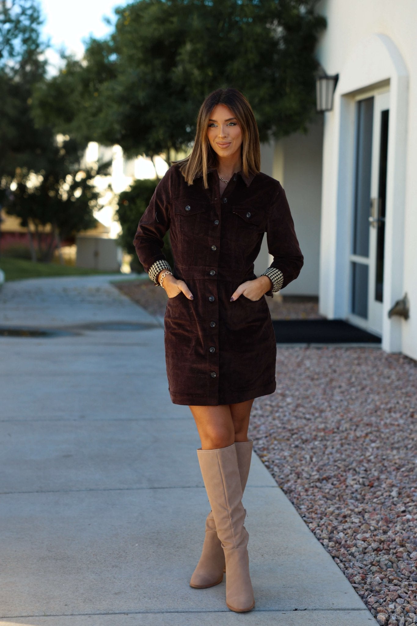 Woman outdoors in the Thread and Supply Brown Corduroy Mini Dress, hands in pockets, near a white building and trees.