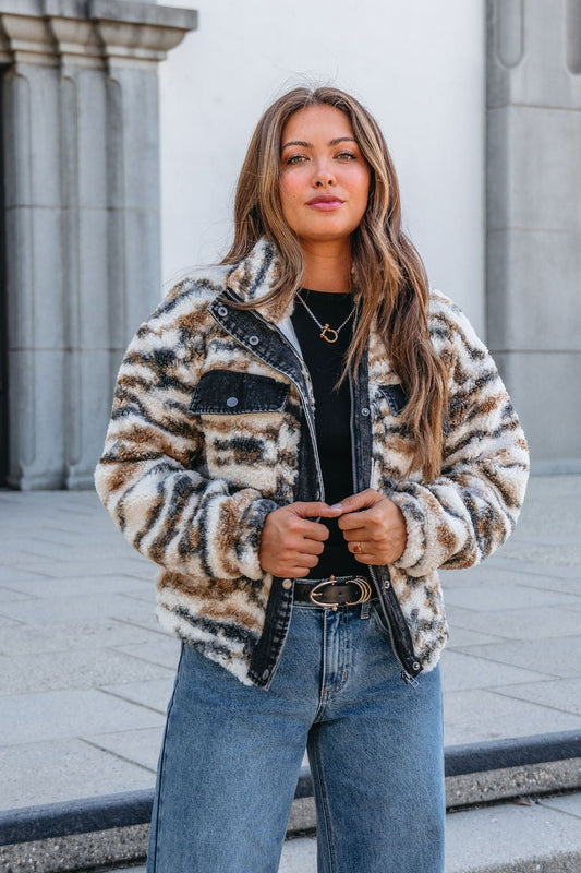 A woman in a Thread and Supply Cream Multi Print Sherpa Jacket stands confidently by a stone building, gazing at the camera.