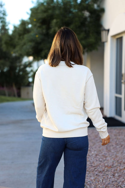 Wearing the Thread and Supply Cream Stitch Buttoned Cardigan, a person with shoulder-length hair stands outdoors, back to the camera.