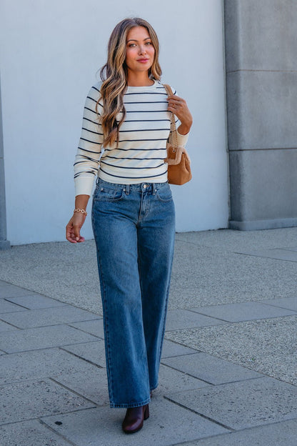 A woman wears the Thread and Supply Ivory Striped Stacy Top with blue jeans and a tan handbag, showcasing her casual style outdoors.