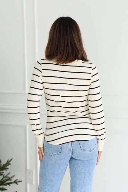 A woman faces away indoors wearing the Thread and Supply Ivory Striped Top with ribbed details and light blue jeans.