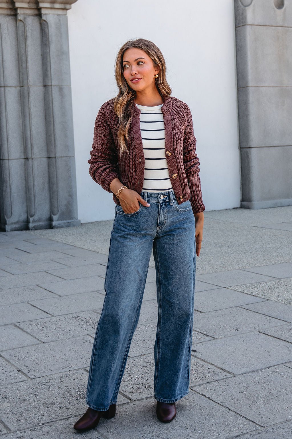 Woman outdoors in a brown cardigan, striped top, Thread and Supply Avery Straight Leg Jeans, and brown boots, looking to the side.