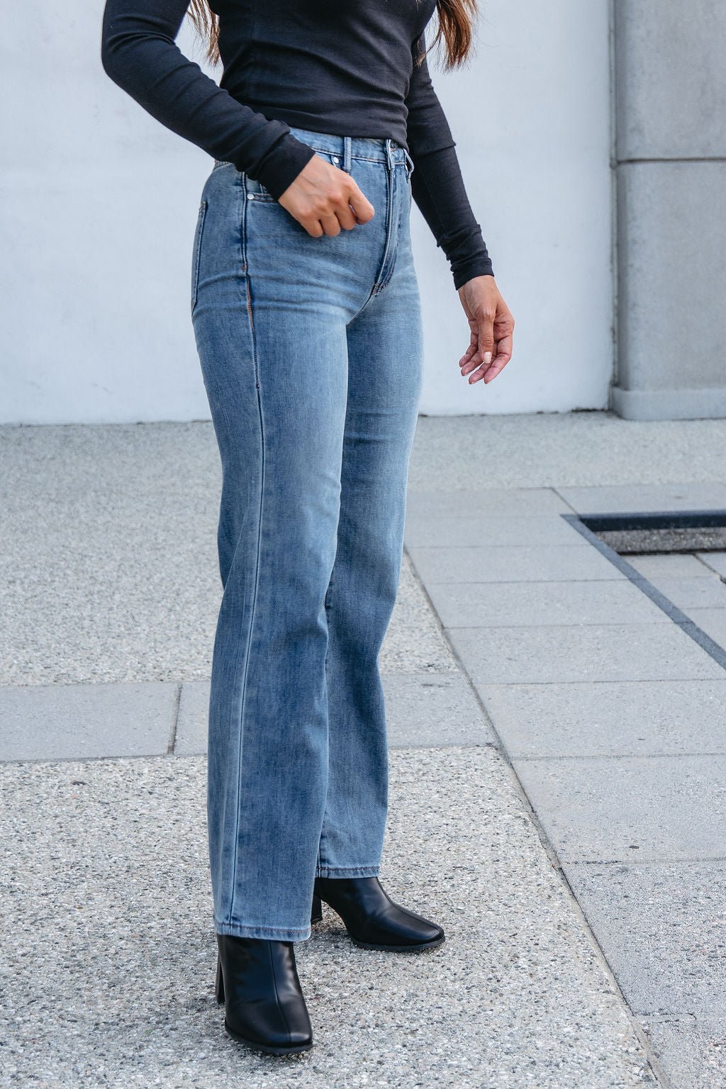 Person wearing Thread and Supply Medium Wash Avery Straight Leg Jeans, black boots, and a long-sleeve black top outdoors.